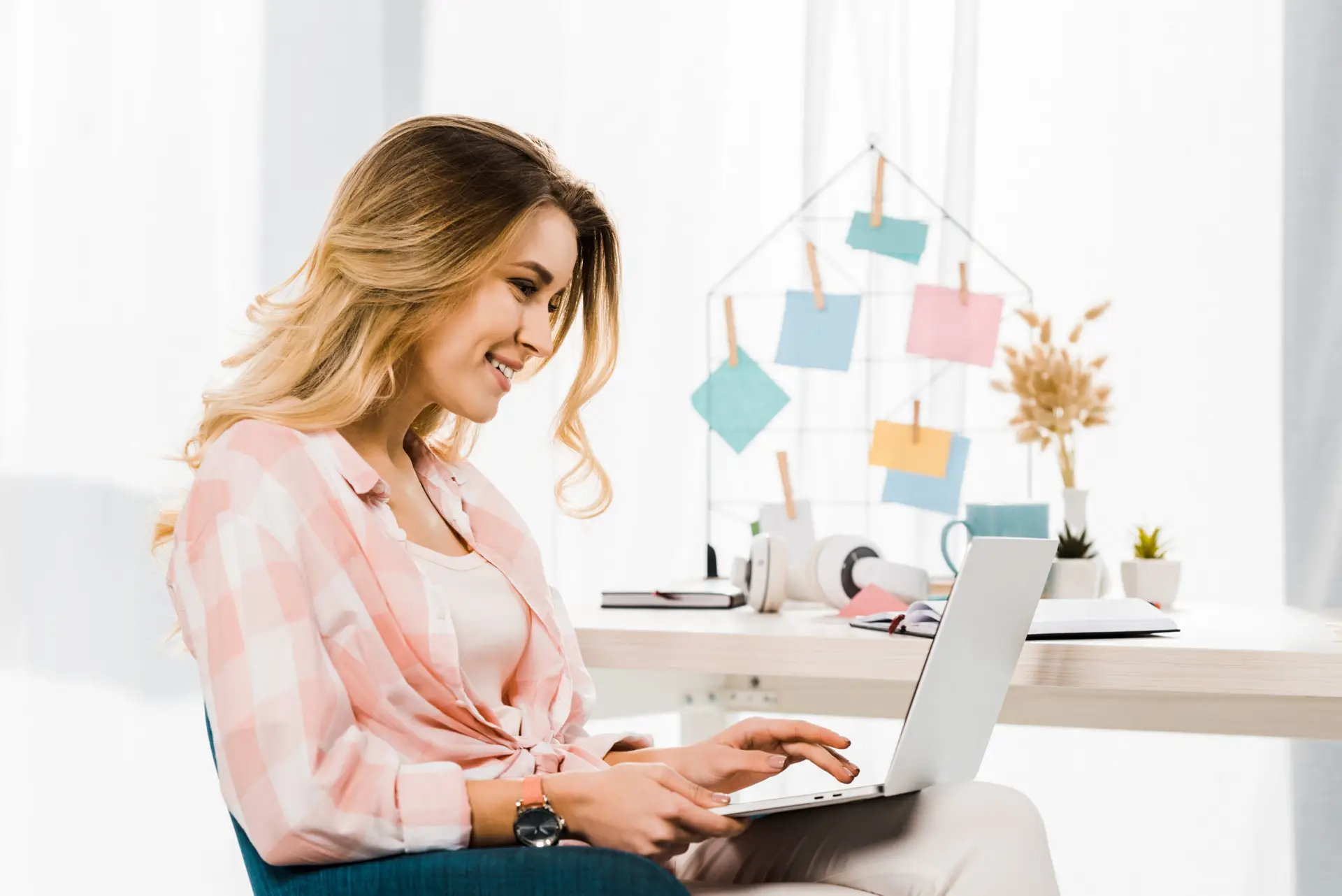 Smiling blonde woman in checkered shirt typing on laptop keyboard